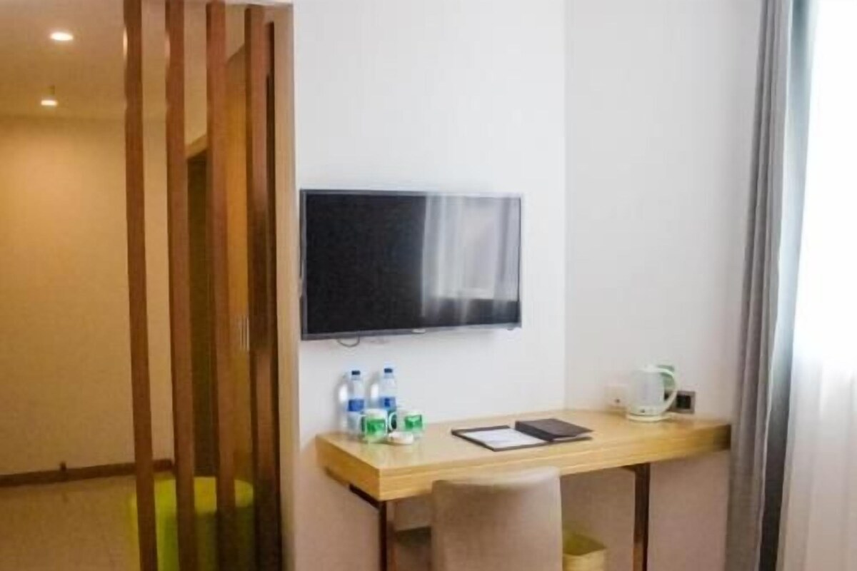 A small room with a desk, a chair, a television mounted on the wall, and a window with curtains.