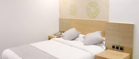 A neatly made bed with a wooden headboard, a bedside table with a lamp, and a green stool.