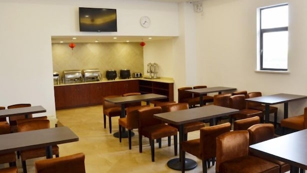 A dining area with tables and chairs, a kitchen area with appliances, and a clock on the wall.