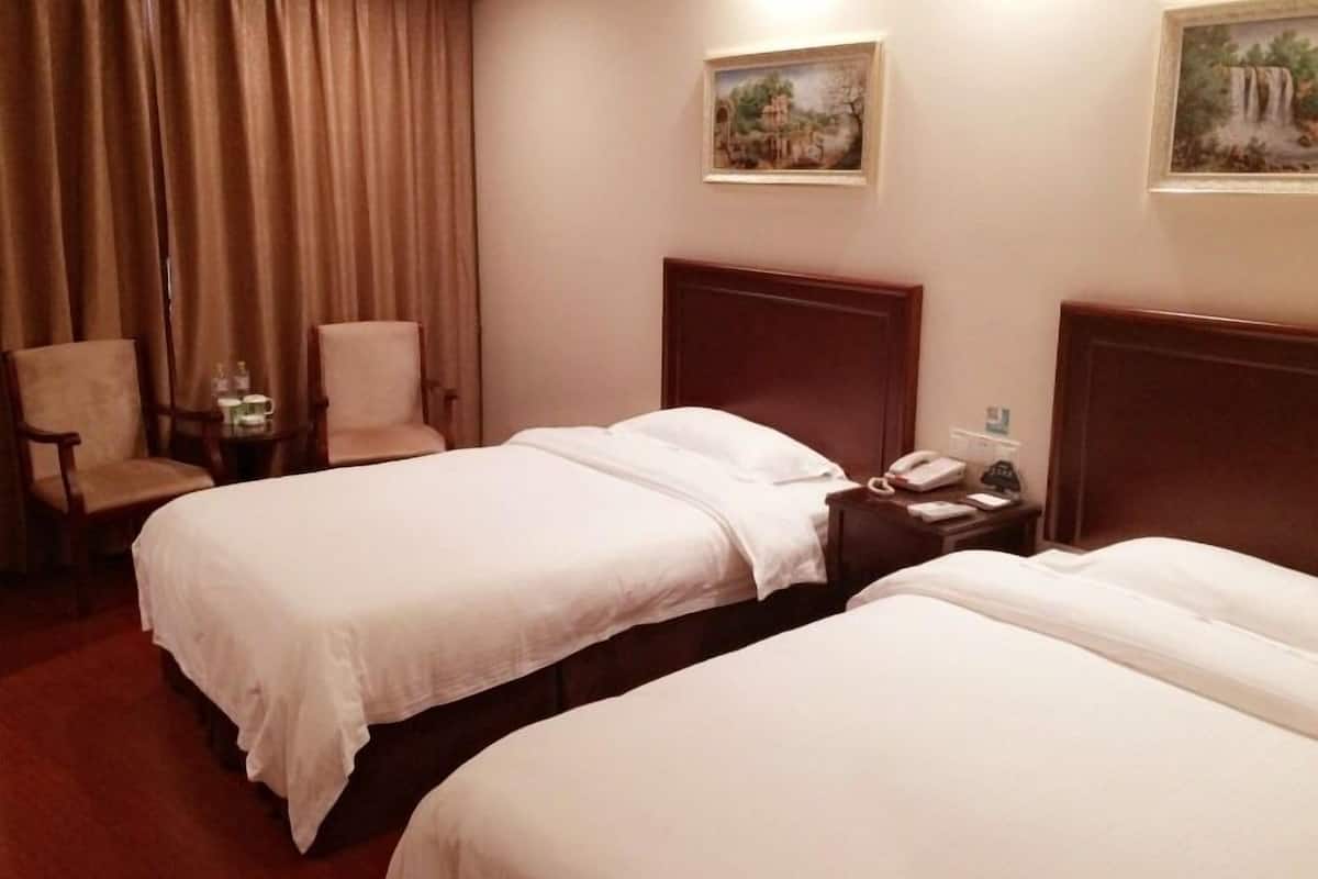 Habitació d'hotel amb dos llits, una cadira, una petita taula de nit amb telèfon i dues pintures a la paret.