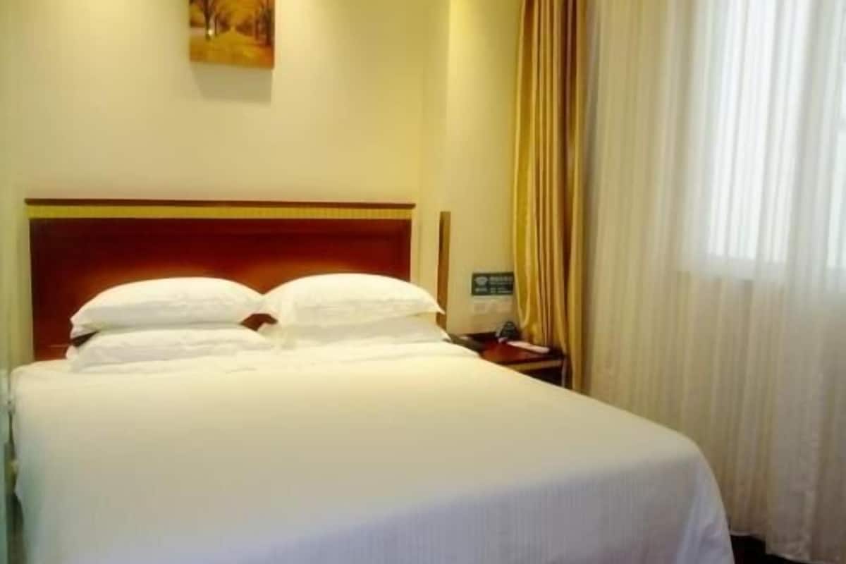 Una habitació d'hotel amb un llit gran, una tauleta de nit, un quadre a la paret i una finestra amb cortines.