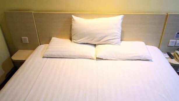 A neatly made bed with white linens and pillows, a bedside table with a lamp, and a wall socket. - Hanting Hotel Ji'nan Baotu Spring (Jinan)
