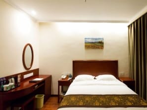 A hotel room with a bed, a desk, a telephone, a trash bin, and a painting on the wall. - Greentree Inn (Xinxiang)