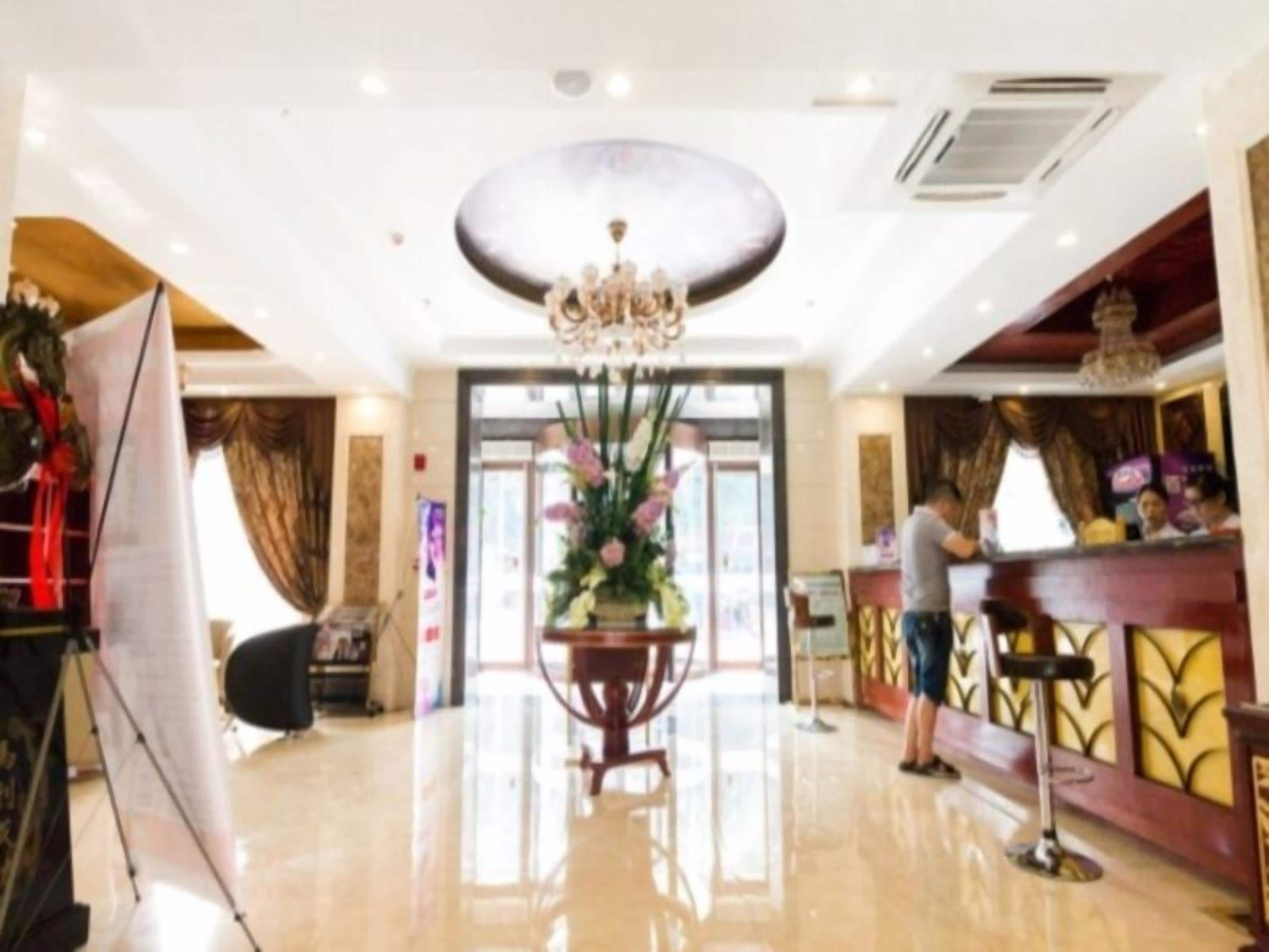 Un hall d’hôtel avec un comptoir d’accueil, un lustre et un grand vase rempli de fleurs.