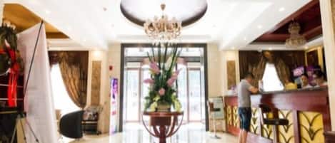 Un vestíbulo de hotel con mostrador de recepción, un candelabro y un gran jarrón de flores.