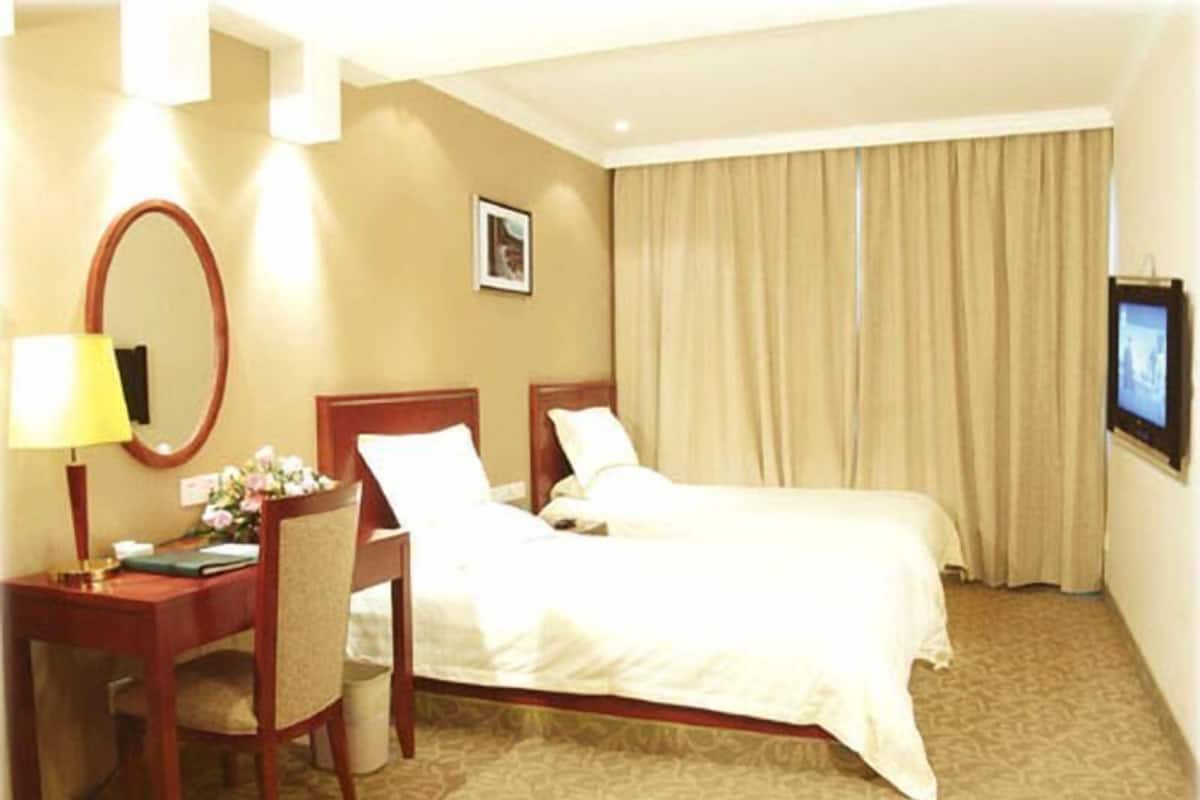 A hotel room with a bed, a desk, a chair, a mirror, a television, and a window with curtains.