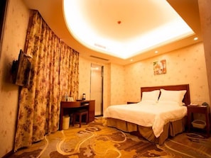A hotel room with a bed, a desk, a television, and a patterned carpet.