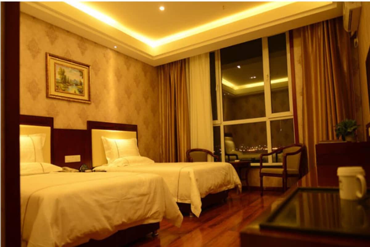 A hotel room with two beds, a desk, chairs, a window with curtains, and a painting on the wall.