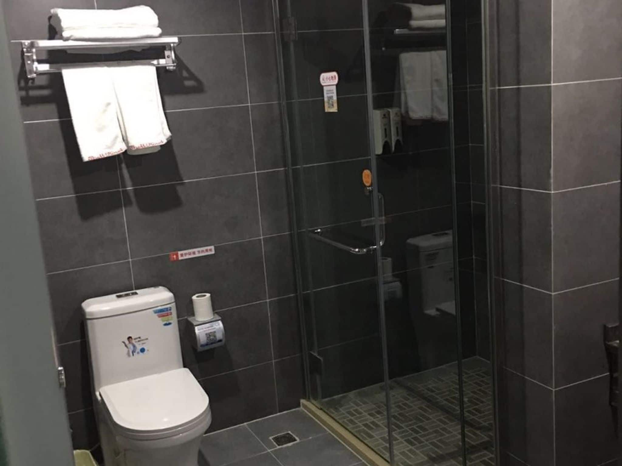 A bathroom with a toilet, a glass shower enclosure, and a towel rack with towels.
