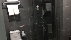 A bathroom with a toilet, a glass shower enclosure, and a towel rack with towels.