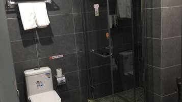 A bathroom with a toilet, a glass shower enclosure, and a towel rack with towels.