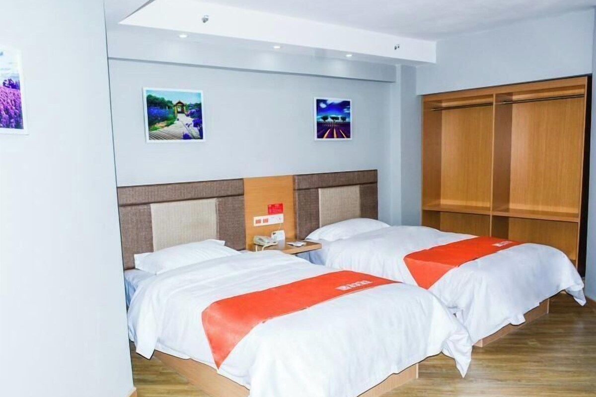 Quarto de hotel com duas camas, um guarda-roupa de madeira e duas molduras na parede.