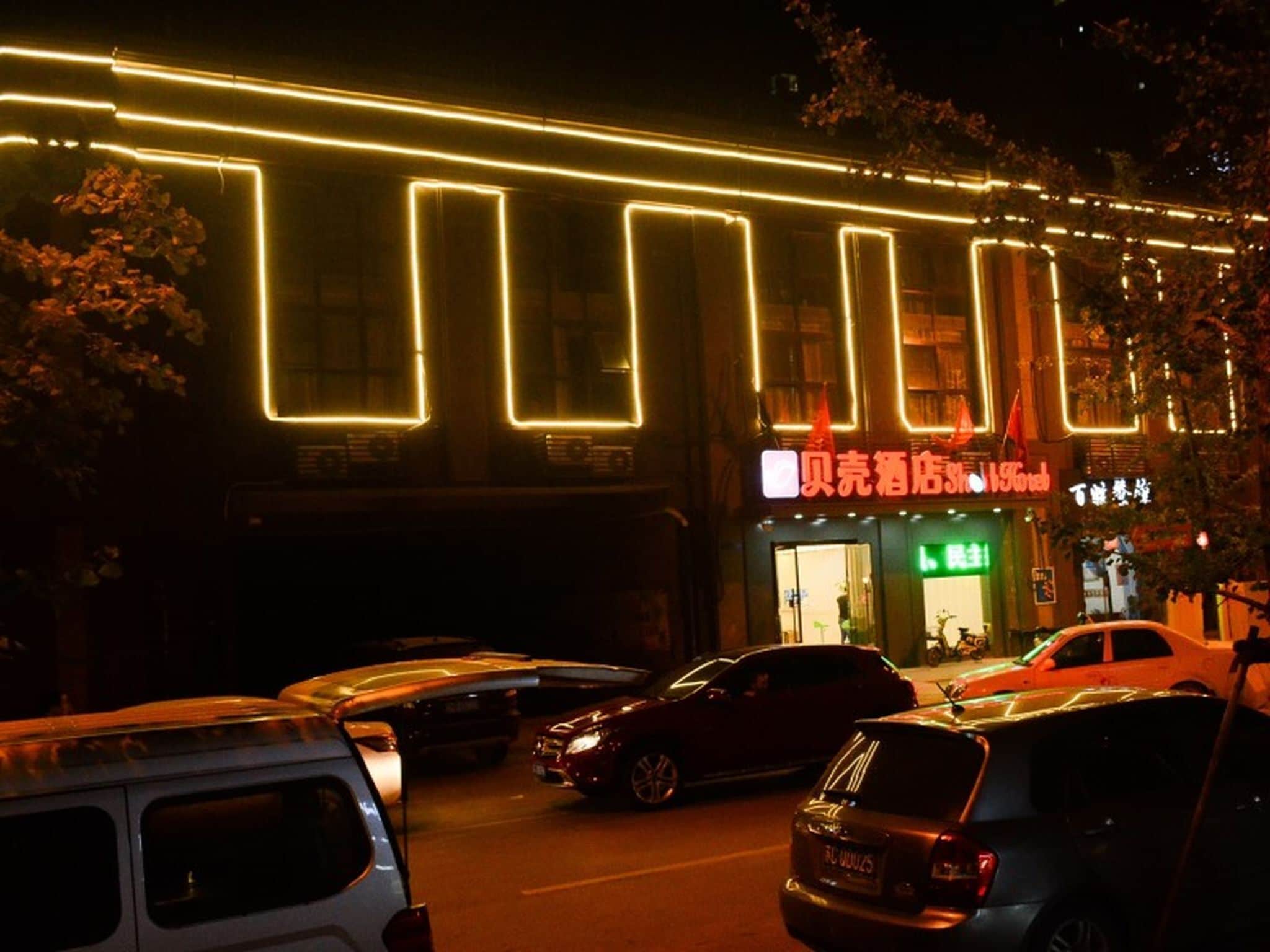 A building with illuminated neon lights, a storefront with signage, and parked cars.
