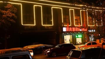 A building with illuminated neon lights, a storefront with signage, and parked cars.