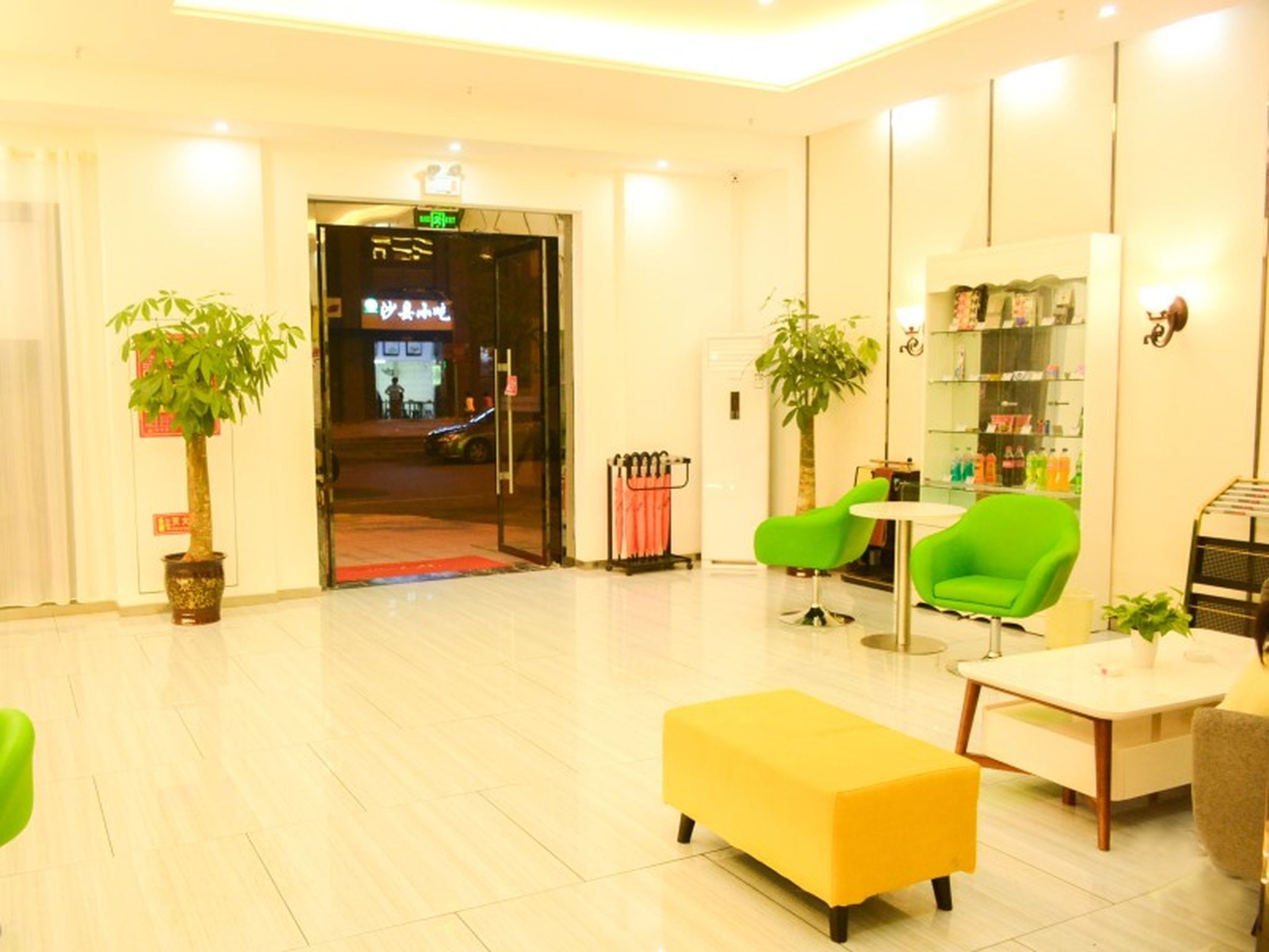 A hotel lobby with a reception desk, green chairs, a yellow sofa, and potted plants.