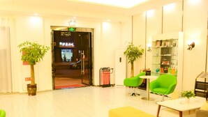 A hotel lobby with a reception desk, green chairs, a yellow sofa, and potted plants.