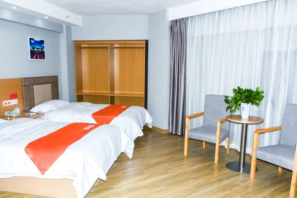 Et hotelværelse med to senge, et træskab, et lille bord med en plante og en stol.