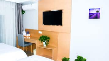 A hotel room with a bed, a desk with a chair, a television mounted on the wall, and a small potted plant on the desk.