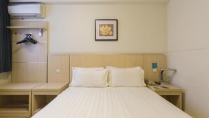 A hotel room with a bed, a bedside table, a hanging coat rack, a wall-mounted air conditioner, and a framed picture. - Jinjiang Inn Wuhan Jiangtan Nanjing Road Science Museum (Wuhan)