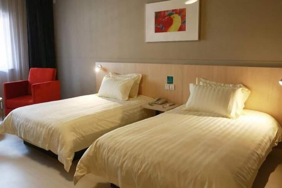 A hotel room with two beds, a red chair, a painting on the wall, and a bedside table with a phone.