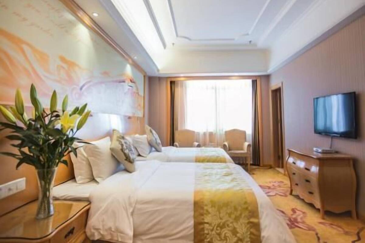 A hotel room with two beds, a TV, a dresser, and a large window.