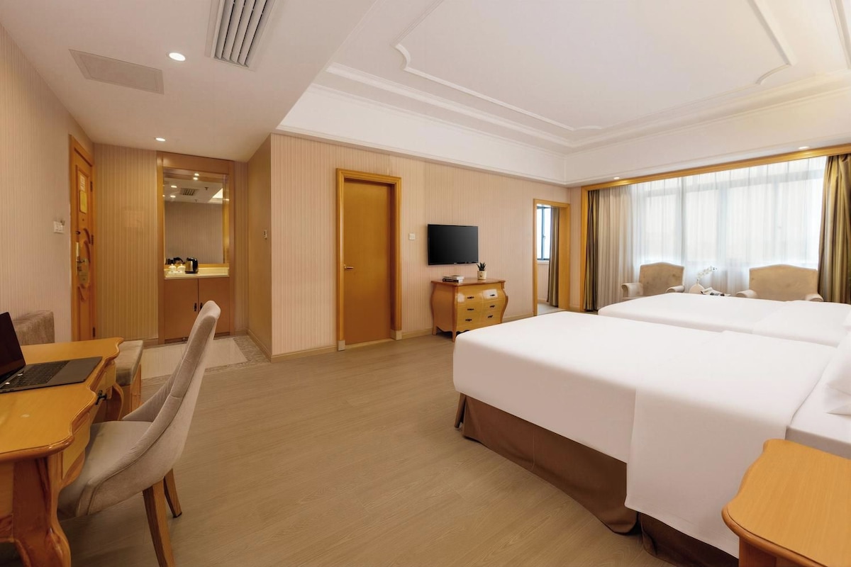 Quarto de hotel com cama, escrivaninha, cadeira, televisão e um pequeno armário.