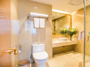 A modern bathroom with a glass shower enclosure, a toilet, a sink with a mirror above it, and a towel rack. - Vienna Hotel (Shaoyang)