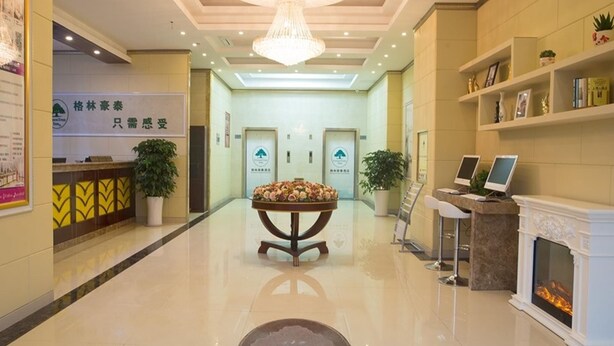 A hotel lobby with a reception desk, a chandelier, a fireplace, and a reception area with a plant. - Greentree (Suzhou)