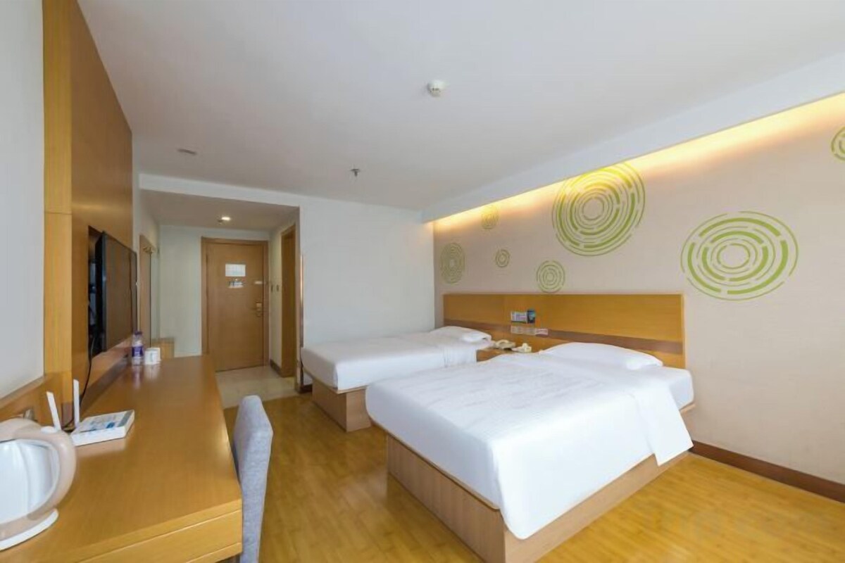 Habitación de hotel con dos camas, un escritorio de madera, una silla, un televisor y un espejo.