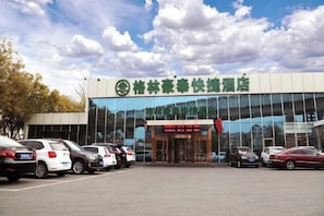 A modern building with a glass facade, a parking lot with several cars, and a sign with Chinese characters. - GreenTree (Beijing Jingzhou Road Magezhuang Subway Station) (Fangshan)