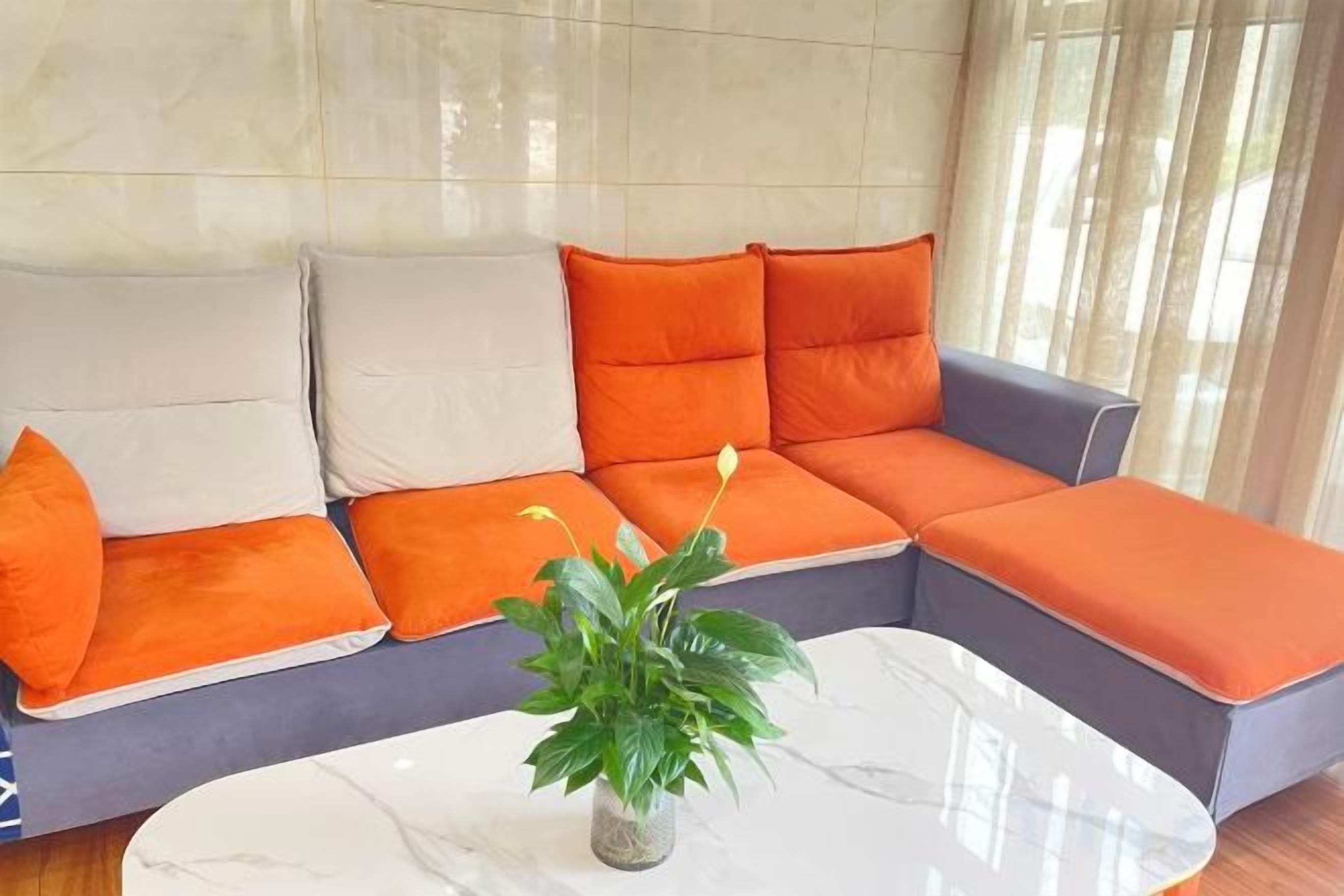 A sectional sofa with orange and white cushions, a marble coffee table, and a potted plant.