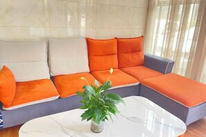 Um sofá modular com almofadas laranja e brancas, uma mesa de centro de mármore e uma planta em vaso.