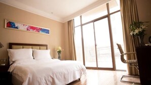 Ein Hotelzimmer mit einem großen Bett, einem Sessel, einem Schreibtisch und einem Vorhangfenster.