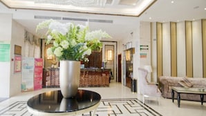 Eine Hotelhalle mit einer Rezeption, einer großen dekorativen Vase mit Blumen, einem runden schwarzen Tisch und einem gemusterten Boden.