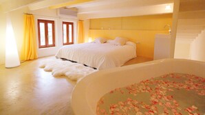 Ein Schlafzimmer mit einem großen Bett, einer Badewanne voller Rosenblätter und einer Treppe.