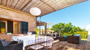 Eine Terrasse im Freien mit Esstisch, Korbmöbeln und einer Pergola darüber.