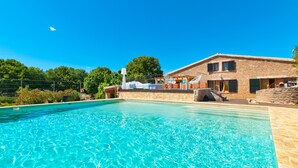 Ein Schwimmbecken mit klarem Wasser, ein Steinhaus mit Balkon und Bäume im Hintergrund.