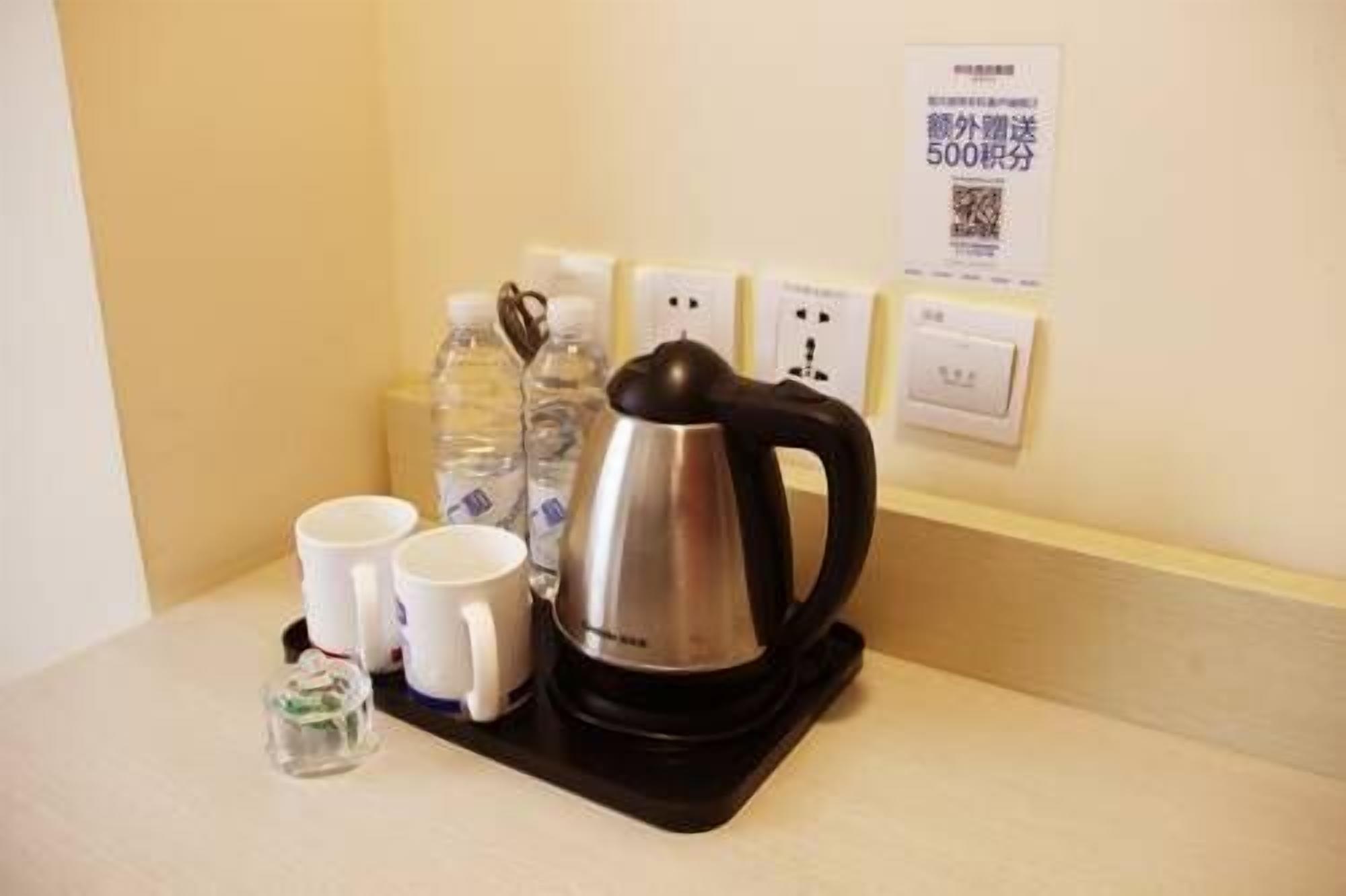 A kettle, two cups, and a water bottle on a table with a power outlet and a sign in the background.