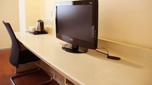 Quarto de hotel com uma escrivaninha, monitor de computador, cadeira e máquina de café.