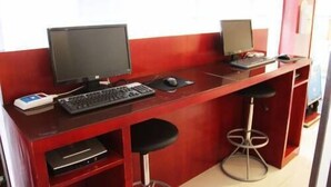 Uma mesa vermelha com um computador, teclado, rato e um monitor pequeno.
