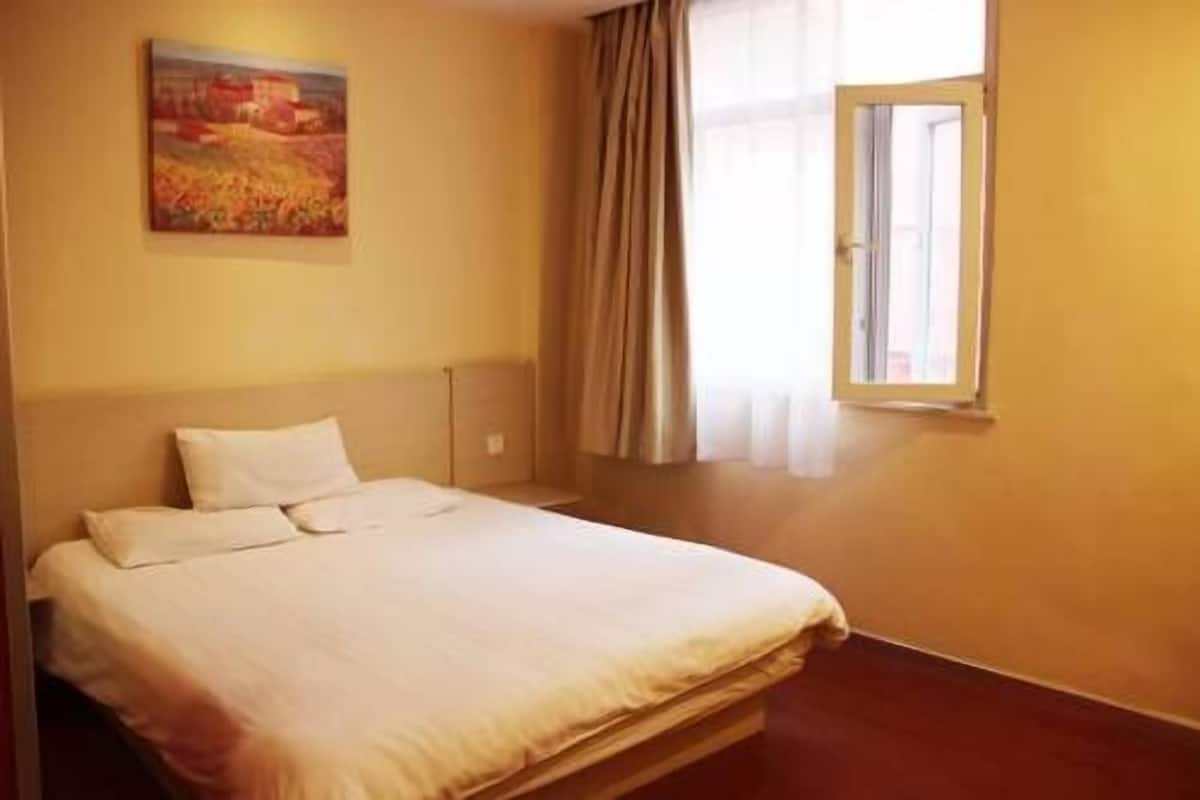 Una habitación de hotel con una cama, un cuadro en la pared y una ventana con cortinas.