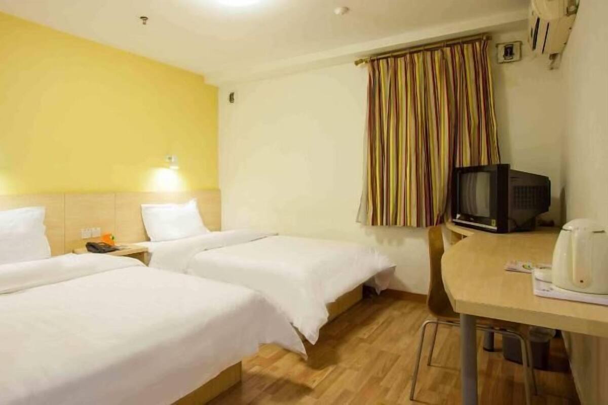 A hotel room with two single beds, a small table with a television, and a window with curtains.
