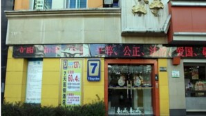Eine Hotelscheibe mit gelb-roter Fassade, einem Schild für ein Gasthaus für 7 Tage und einem sichtbaren Eingang mit Glastür.