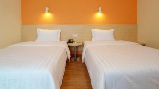 Ein Hotelzimmer mit zwei Einzelbetten, einem kleinen Nachttisch und einer Wandleuchte.