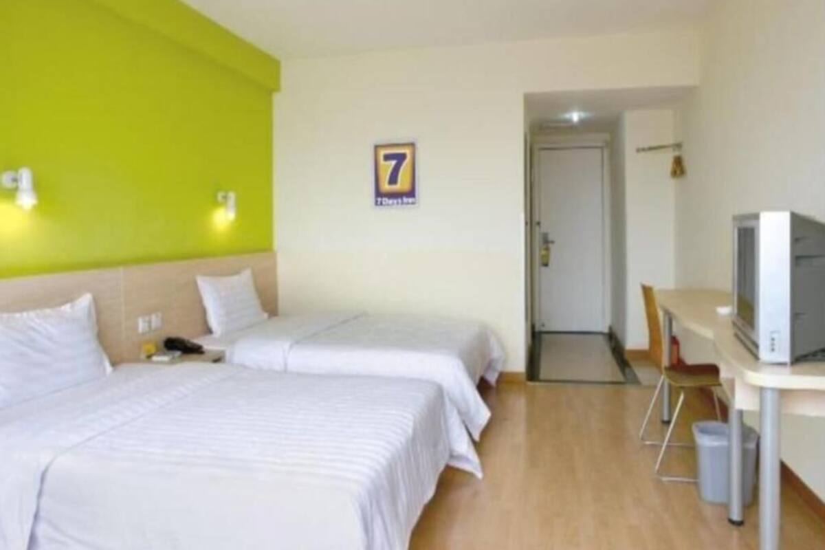 A hotel room with two beds, a television, and a door leading to a hallway.