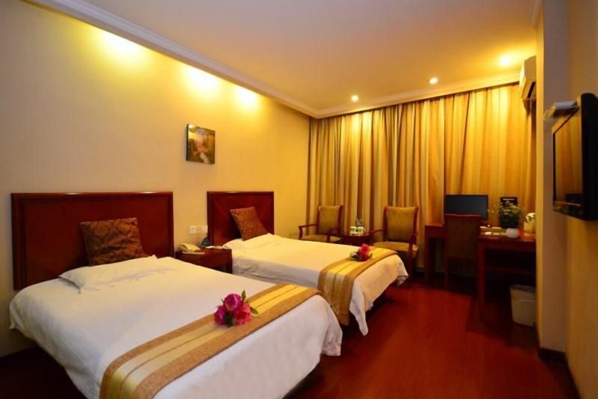 A hotel room with two beds, a desk, a chair, a TV, and a window with curtains.