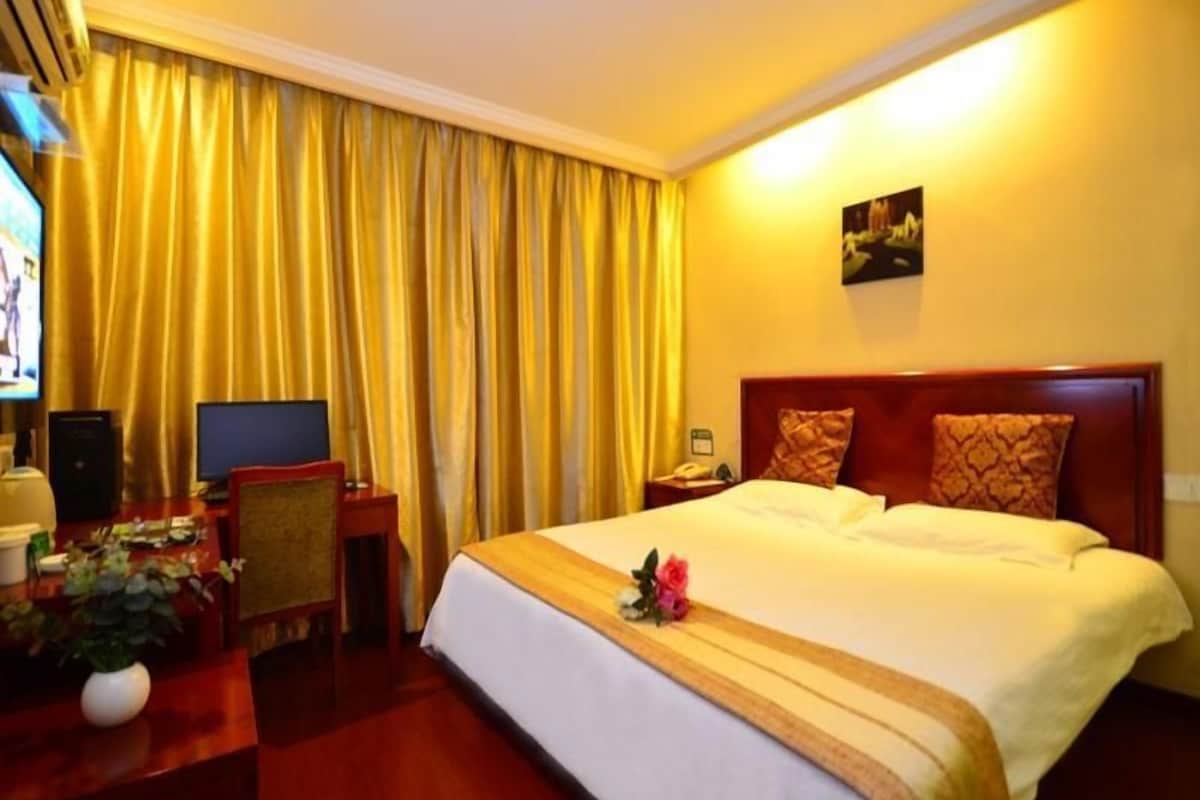 A hotel room with a large bed, a desk with a computer, a TV, and a plant.