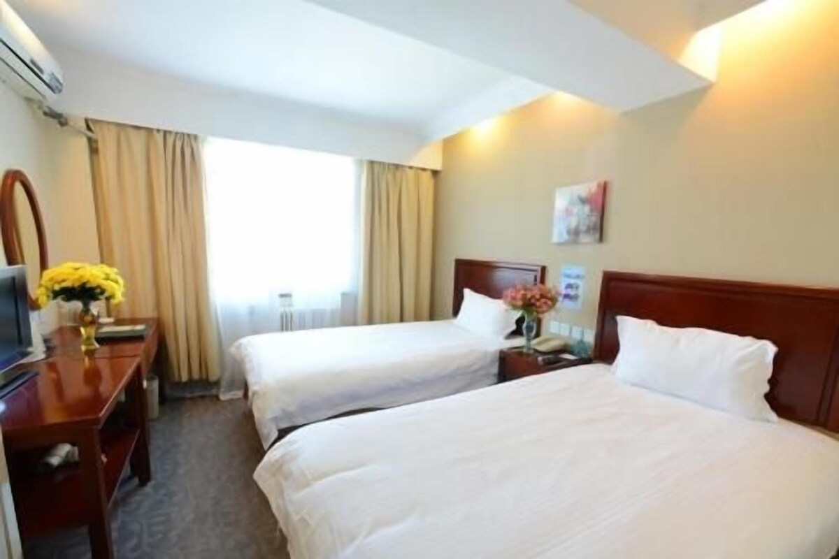 A hotel room with two beds, a desk, a chair, a TV, and a window with curtains.