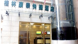 A hotel entrance with a glass door, a reception desk inside, and a flag above.