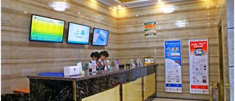 A reception desk with digital displays, a marble counter, and informational posters.